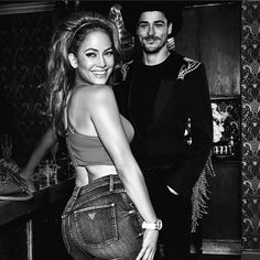 a man and woman standing next to each other in front of a bar with drinks