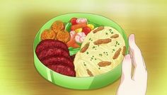 a green bowl filled with food on top of a wooden table next to someone's hand