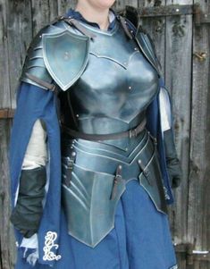 a woman dressed as a knight standing in front of a wooden fence with her hands on her hips