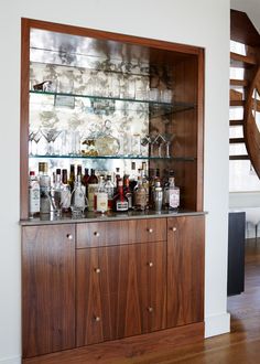 a wooden cabinet filled with bottles and glasses on top of a hard wood floor next to a spiral staircase