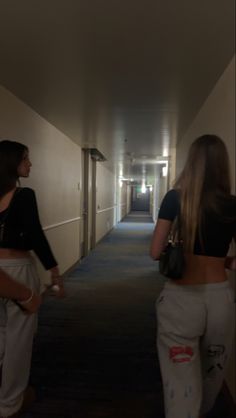 two women walking down a long hallway in white sweatpants and black cropped tops