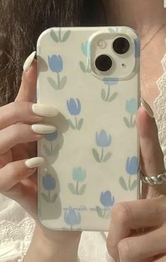 a woman holding up her phone case with blue flowers on the front and back cover