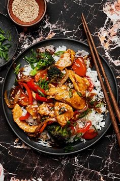 a black plate topped with chicken, broccoli and rice next to chopsticks