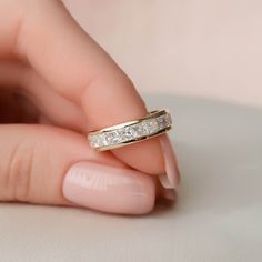 a woman's hand holding a wedding ring with three diamonds on it and the band is gold