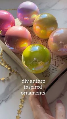 a person touching some soap balls on top of a book with the words diy anthro inspired ornaments