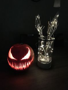 a lighted pumpkin sitting next to a vase filled with branches