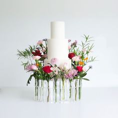 a white cake with flowers in vases sitting on a table next to a candle