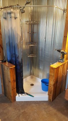 a bathroom with a stand up shower next to a blue bucket and wooden stools