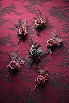 several small boutions are arranged on a red tablecloth with black lace and flowers