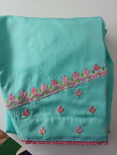 two pieces of blue cloth with pink flowers and green leaves on the edges, one piece has been embroidered