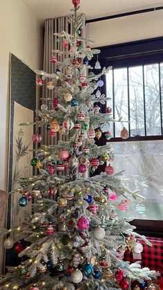 a white christmas tree with colorful ornaments in front of a window and plaid table cloth