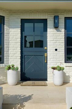 two large white planters with plants in front of a blue and white house door