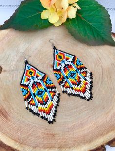 the beaded earrings are sitting on top of a piece of wood next to a flower