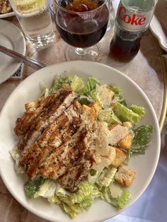 a white plate topped with salad and meat next to two glasses of coke on a table