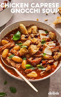 chicken caprese gnocchi soup in a white bowl with spoon and bread croutons on the side