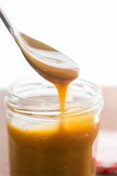 a spoon full of caramel sauce being poured into a jar