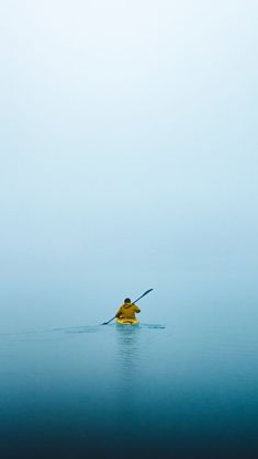 a person in a yellow kayak paddling through the water on a foggy day