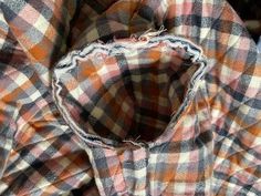 an orange and black checkered shirt with holes in the middle, sitting on top of a pile of other clothing