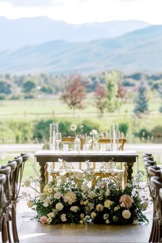 the table is set up with flowers and greenery for an outdoor wedding reception in front of mountains