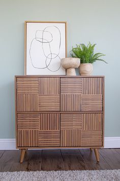 a wooden cabinet sitting next to a plant on top of a hard wood floor