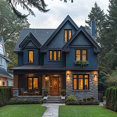 a large house with lots of windows and lights on it's front porch, surrounded by greenery