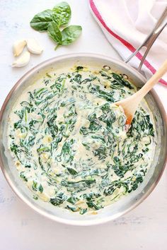 spinach and cheese sauce in a pan with a wooden spoon next to it on a white surface