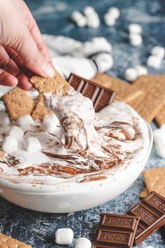 a person dipping marshmallows into a bowl of s'mores dip