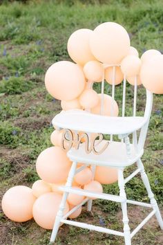 a white chair sitting on top of a field filled with lots of peach colored balloons