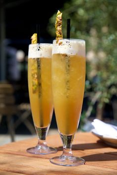 two glasses filled with drinks sitting on top of a wooden table