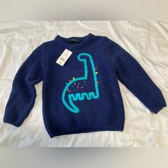 a blue sweater with a dinosaur drawn on the front and back, sitting on a white sheet