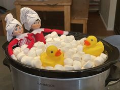 two elfs are sitting in a crock pot filled with marshmallows