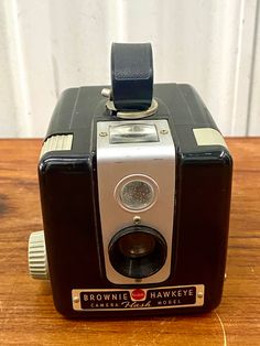 an old brownie hawkeye camera sitting on a wooden table next to a wall