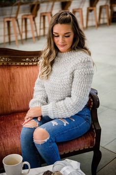 a woman sitting on top of a wooden bench next to a coffee cup and paper