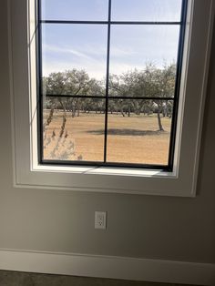 an empty room with a large window looking out at the field outside and trees in the distance