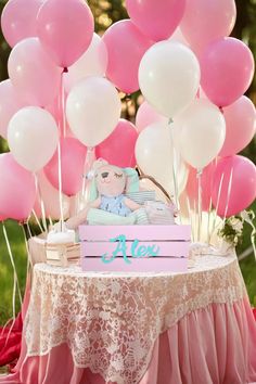 a table topped with pink and white balloons next to a cake on top of a wooden box