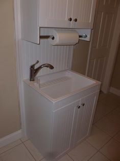 a white bathroom sink sitting under a cabinet next to a toilet paper roll dispenser