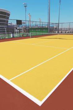 the tennis court is painted yellow and red with white lines on it, as well as a large building in the background