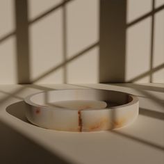 a white bowl sitting on top of a table next to a window with the light coming through it