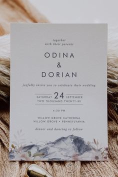 a white wedding card on top of a fur coat with a mountain scene in the background