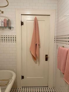 a bathroom with black and white tile flooring and pink towels hanging on the door