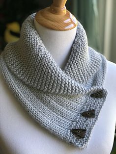 a white mannequin wearing a gray knitted cowl with buttons on it