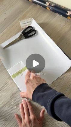 a person is cutting paper on top of a table with scissors and papers in front of them