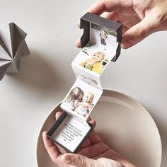 a person holding an origami photo frame over a plate with two photos on it