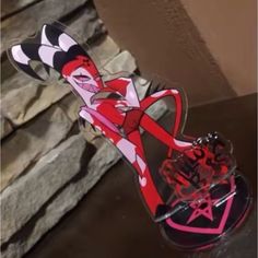 a pair of red and black high heels sitting on top of a wooden table next to a stone wall