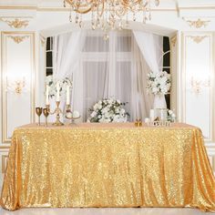 the table is covered with pink sequins and white flowers in front of a chandelier