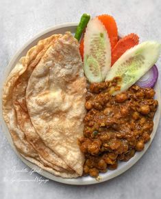 a white plate topped with meat and veggies next to pita bread on top of a table