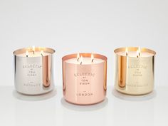 three different colored candles sitting next to each other on a white surface with one candle lit