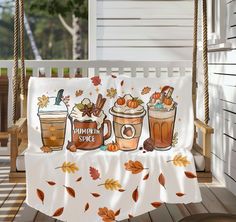 a porch swing with two cups of coffee on it and fall leaves around the table