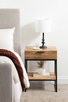 a nightstand with a lamp on it next to a bed