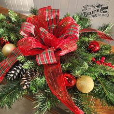 a christmas wreath with red and green ribbon, pine cones, ornaments and ribbons on it